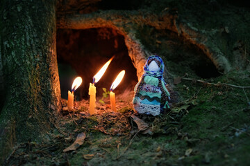 witchcraft foll doll and burning candles in dark forest. magic guardian spirit of nature. ancient...