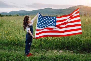 Close up of playful happy little preschool girl with national USA flag outdoors at summer on background summer green mountains. American flag, country, patriotism, independence memorial day 4th July
