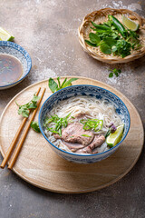 Traditional vietnamese noodle soup pho in bowl, garnished with basil, mint, lime, on concrete background - obrazy, fototapety, plakaty