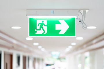 A Arrow light box sign of EMERGENCY FIRE EXIT is hung on the ceiling in hospital walkway, Idea for event fire or evacuation drills. - Powered by Adobe