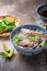 Close view of pho bo in traditional bowl, garnished with basil, mint, lime, on concrete background - 438573893