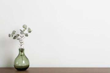 Empty home desk table background. Wooden table with a vase and a plant against a white wall in the...