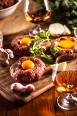 Beautifully prepared beef steaks tartare with appetizing egg yolks. Served with garlic, onion, herbs and alcohol as a beverage. White bowl full of raw meat in the background