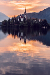 Fototapeta na wymiar Lake Bled in Slovenia viewed from the ground showing the pilgrimage church at sunrise in beautiful orange colors