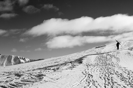 Skier with skis go up to top of mountain. Black and white toned image. High contrast.