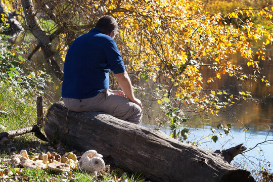 Man sitting with his back on wooden log by river