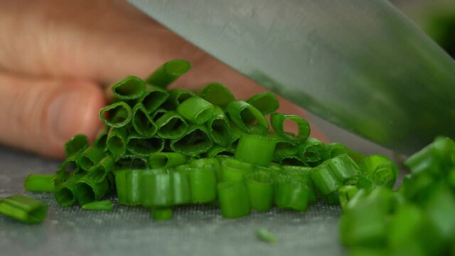 Close up of male chefs hands cut fresh green onions with kitchen knife. Cooking concept with greens. Green vegetables, herbs