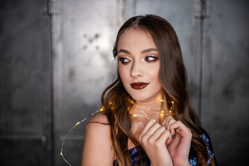 Close-up portrait of beautiful girl with an evening festive, professional make-up, bright, shiny garland around neck. Dark metallic background. Grunge texture of loft interior. Clean skin healthy face