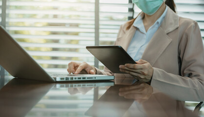Women are using tablet and laptop computer to work at the desk in the morning.