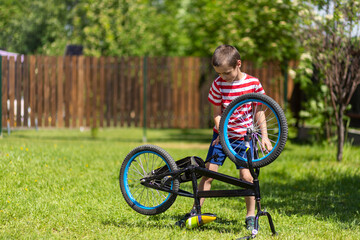 The boy takes his bike very seriously and repairs it alone in garden. Cycling club for children. Little bicycle mechanic at work.