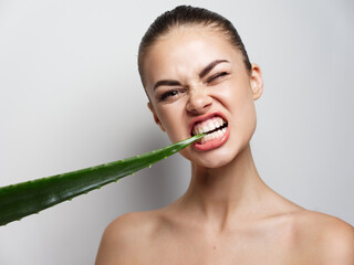 emotional woman with bare shoulders gnaws a green leaf on a light background hairstyle model