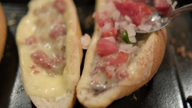 Spoon adding pico de gallo to traditional Mexican molletes above black tray