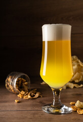 light beer unfiltered with a large strong white foam on a wooden background, copyspace. With beer snacks