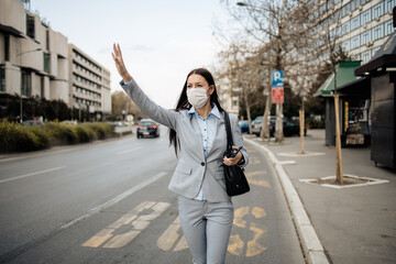 Elegant business woman with protective mask standing alone on empty street and waiting for bus or taxi transport. Corona virus or Covid-19 lifestyle concept.