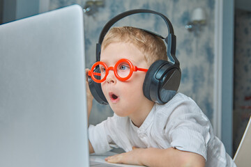 Cute child in red glasses and headphones has fun communicating online via video link using a...