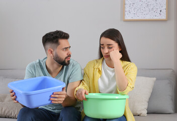 Young couple collecting leaking water from ceiling at home. Time to call roof repair service