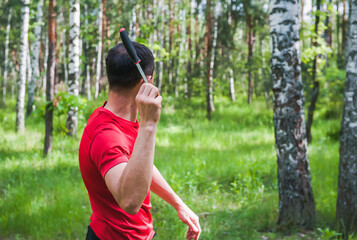 A man throws a knife at a target in the summer forest, back view. Throwing a knife