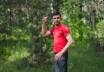 A man throws a knife at a target in the summer forest, front view. Throwing a knife
