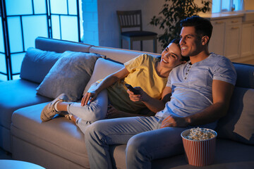Couple watching movie with popcorn on sofa at night