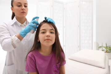 Doctor using lice treatment spray on little girl's hair indoors