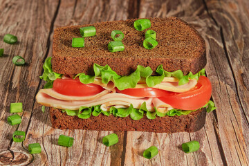 sandwich with black bread, tomatoes and sausage lies on a table made of rough boards, rustic style, organic food