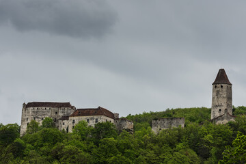 Fototapeta na wymiar old castle with a tower between many green trees and grey sky