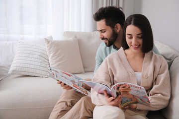 Young couple reading modern magazines on sofa at home, space for text