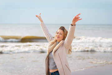 Relaxed woman, arms rised, enjoying spring sun, on a beautiful beach. Young lady feeling free, relaxed and happy.