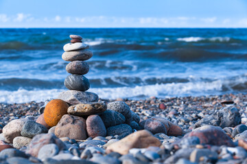 Fototapeta na wymiar Pebble Stone Tower at Sea Shore / Natural stones stacked in balance at windy shore and sound of the sea waves (copy space)