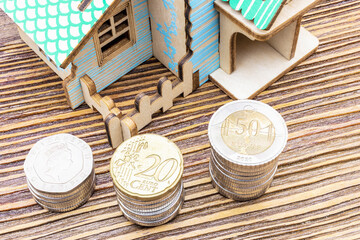 The concept of mortgage, sale and rental of housing and real estate. Buying a home. A mock house with stacks of coins in the foreground on a wooden surface. Banner format. Copy space.