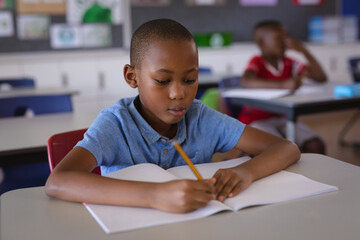African american boy studying while sitting on his desk in the class at school