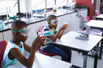 Two african american boys wearing protective glasses holding a beaker in science class at laboratory