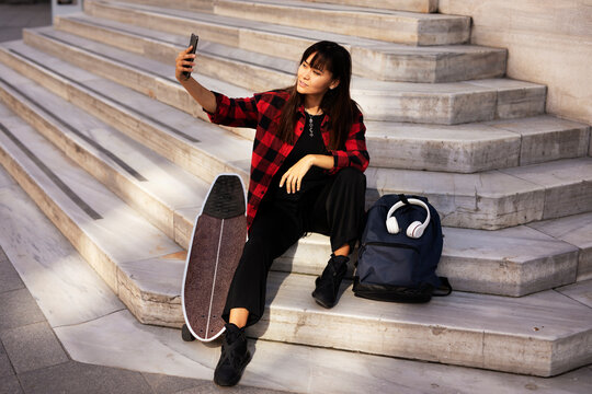 Portrait of young beautiful girl with skateboard. Happy smiling woman taking selfie photo