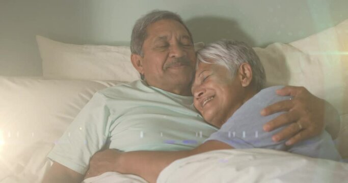 Animation of glowing lights over happy senior couple lying in bed in background