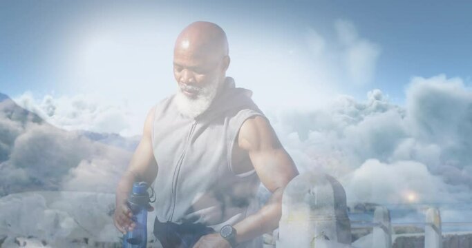 Animation of glowing lights over fit senior man drinking water during exercise and clouds background
