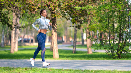 Fototapeta premium Full length photo of a woman running in park in early morning. Attractive looking woman keeping fit and healthy. Format 16x9.