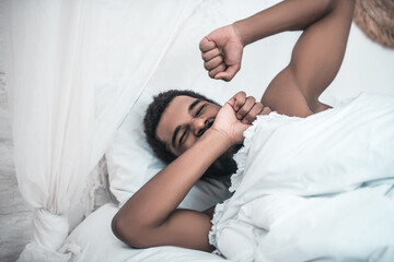 Sleepy yawning darkskinned man in white bed