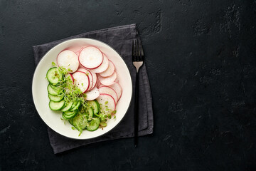 Fresh salad with red radish, cucumber, vegetables, microgreen radishes in white plate on grey stone background. View from above. Concept vegan and healthy eating.