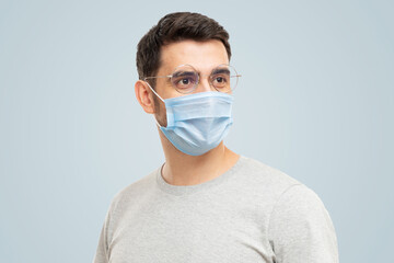 Young handsome man wearing t-shirt, glasses and medical mask looking away, standing isolated on blue background
