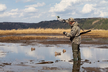 Naklejka premium the hunter stands on the muddy shore of the lake and sets up duck decoy