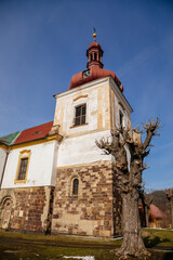 Fototapeta na wymiar White and yellow baroque church of St. Lawrence with bell tower and red dome, clock at tower, sunny winter day, blue sky, Kostomlaty pod Milesovkou, Czech Republic