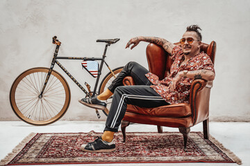 Expressive and stylish guy in hawaiian shirt and sunglasses relaxing on a luxury retro sofa looks...