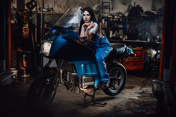 Fototapeta na wymiar Beautiful brunette female mechanic smoking a cigarette while sitting on sportbike in garage