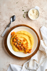 Polenta with butter, pumpkin, garlic, savory and parmesan cheese in white bowl on light concrete background. Traditional Basic Italian food, vegan food. Top view. Copy space.