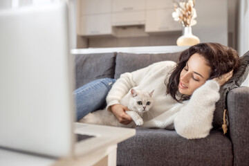 Young woman laying on the sofa with her cat and looking relaxed