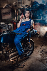 Obraz na płótnie Canvas Female mechanic relaxing smoking a cigarette while lying on custom bobber in garage or workshop
