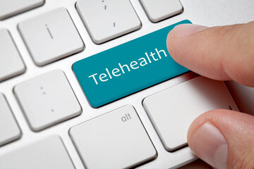 Close-up view on conceptual keyboard - Telehealth, blue key.Male hand pressing telehealth text key on computer keyboard