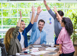 Multiracial diverse cheerful casual businesspeople smiling with happiness, team meeting, raising hands together to celebrate and congratulate successful job progress while sitting in modern company.