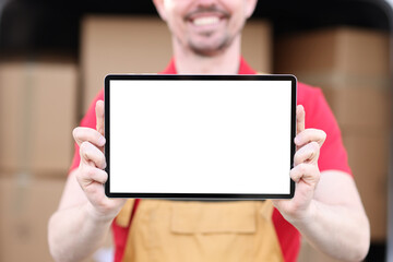 Smiling man in uniform holds tablet with white screen in background of cardboard boxes