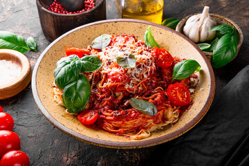 Italian pasta with tomato sauce, tomatoes, cheese and basil on a dark table close up